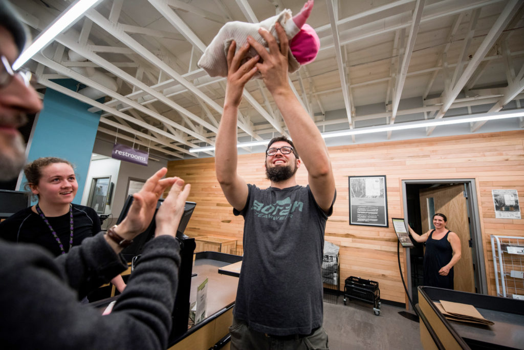 Man presents his baby at the cash register, while mother looks on.
