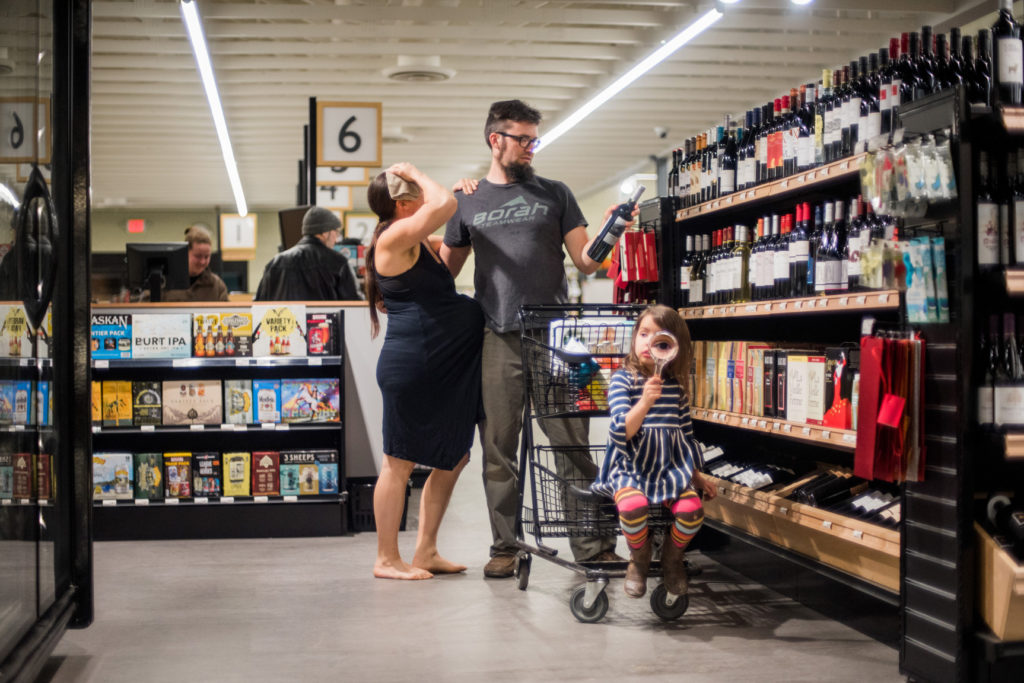 Woman in labor at the co-op, while man looks at wine.
